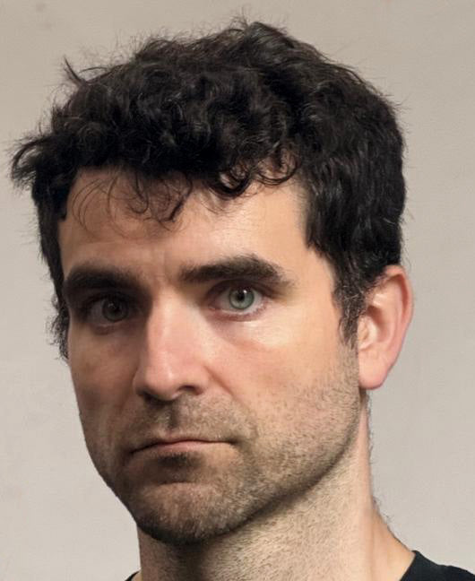 John with a neutral expression in a photograph taken through a mirror
