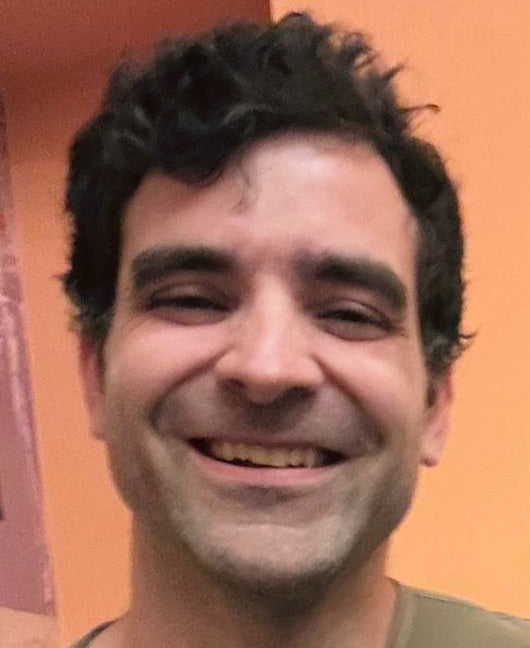 John smiling in a close phone selfie taken from the corner of the original frame